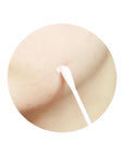 A cotton swab dipping into the pink sediment at the bottom of the bottle, applying the soothing treatment to a targeted acne spot on the skin.